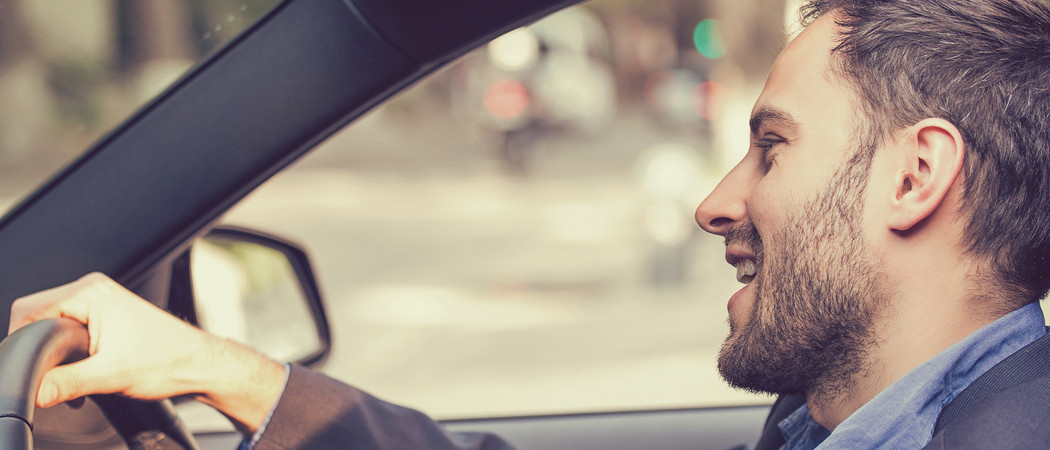 Junger Mann sitzt fröhlich am Steuer eines Gebrauchtwagen - sorgenfrei beim privaten Autoverkauf.