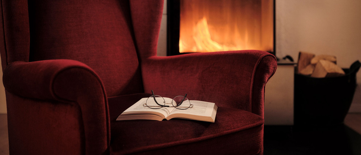 Roter Sessel mit Samt-Polsterbezug vor einem Kamin mit Buch und Brille