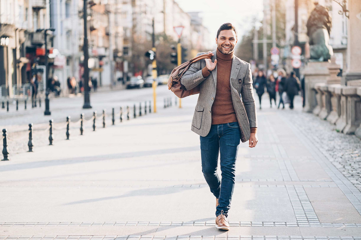 Mann in Jeans, Rollkragenpullover und Sakko läuft durch eine Fußgängerzone