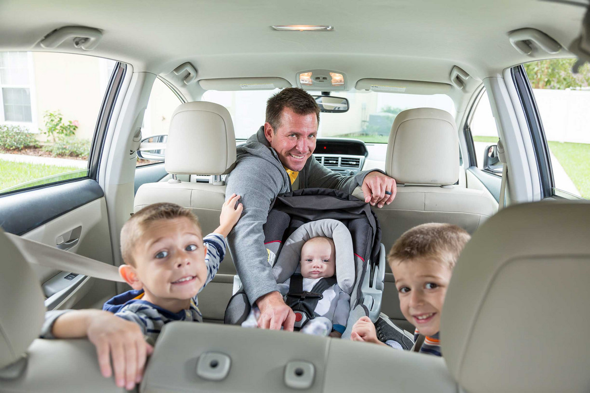 Ein Mann mit Kindern und einem Baby in einer Babyschale im Auto
